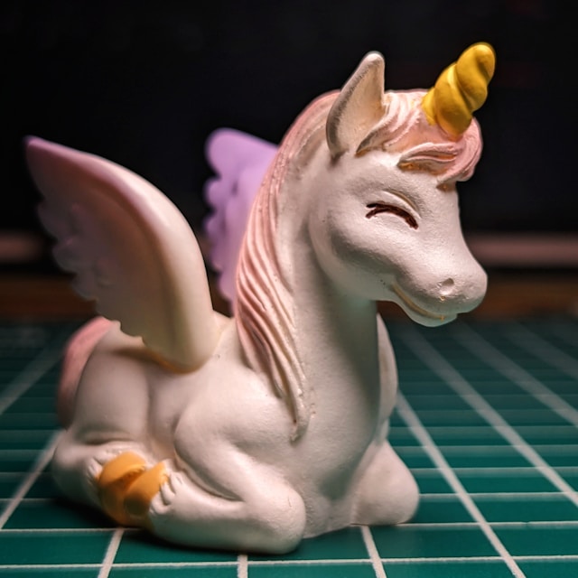 A smiling figurine of a unicorn with wings, kneeling on a table with a grid laid over it
